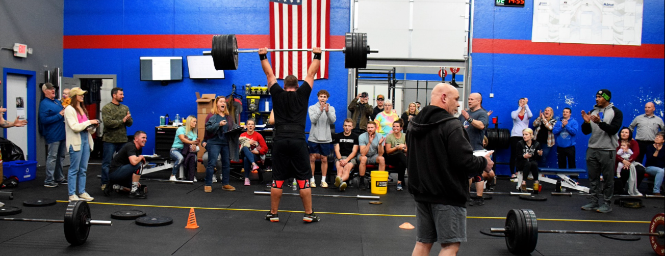 A man is lifting a barbell over his head in a gym.