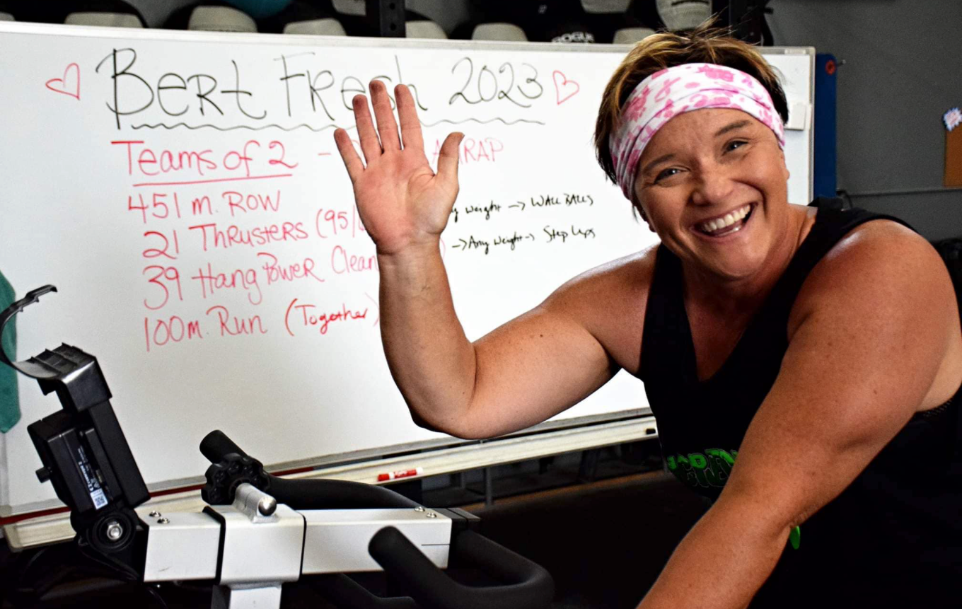A woman is riding an exercise bike in front of a white board