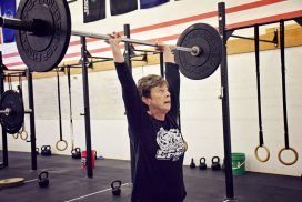A woman is lifting a barbell over her head in a gym.