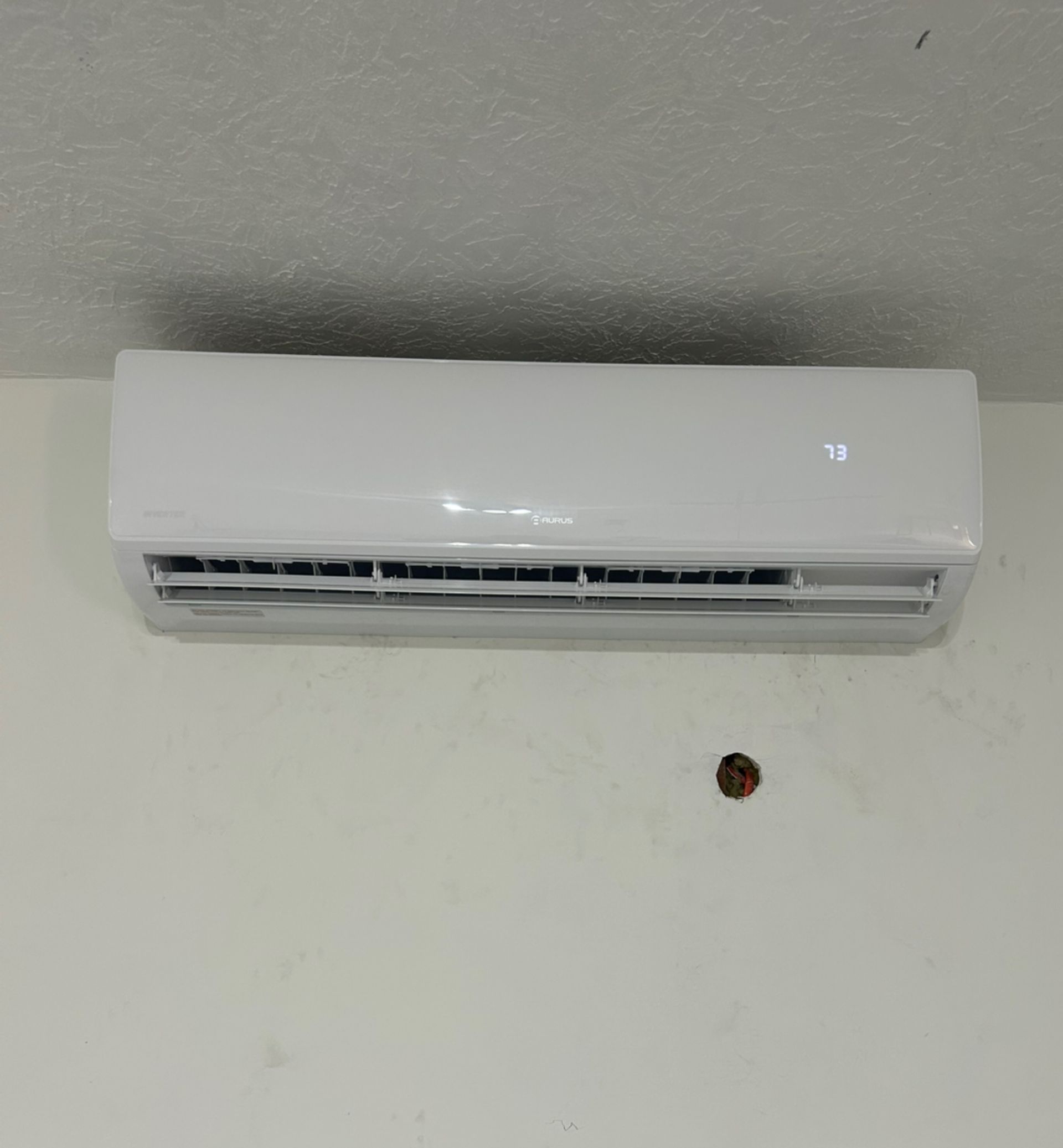 White wall-mounted air conditioner unit. A small, dark stain is below it on the white wall.