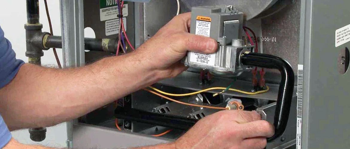 A person is holding a component in a furnace. They are working on the internal mechanisms of the furnace.