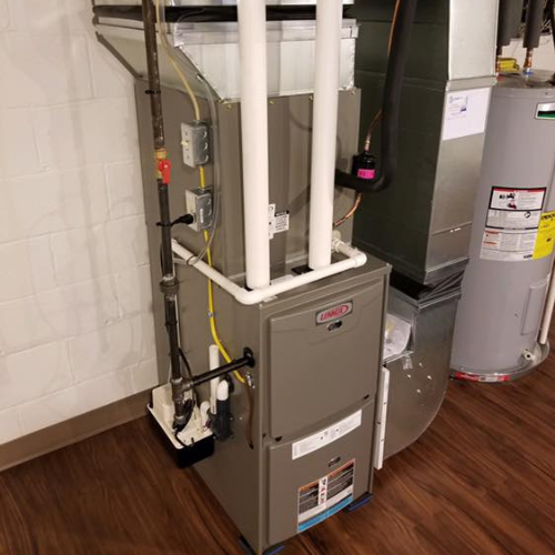 Furnace and water heater in a basement with white pipes and wooden flooring.