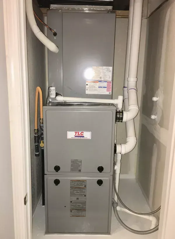 Furnace in a utility closet with vent pipes, gas line, and white painted walls.