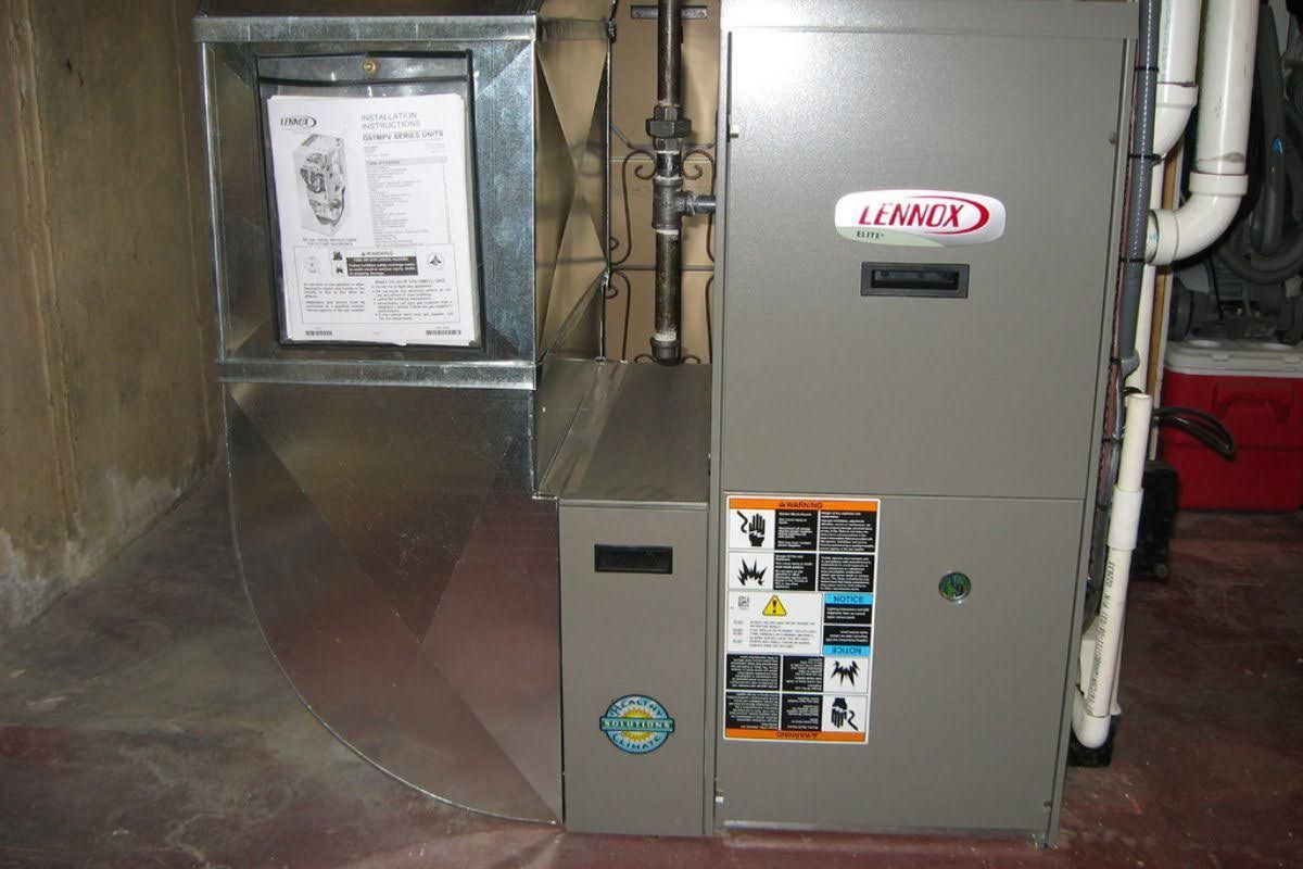 A Lennox furnace in a basement. The unit is gray with multiple labels.