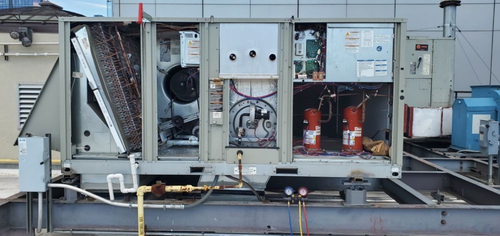 An open air conditioning unit on a rooftop, showing internal components. Gray unit with red tanks and copper coils.