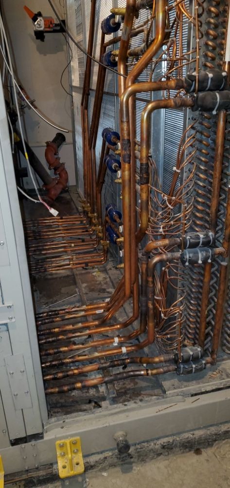 Copper pipes in a mechanical room, arranged with valves and fittings. Some black debris on the floor.