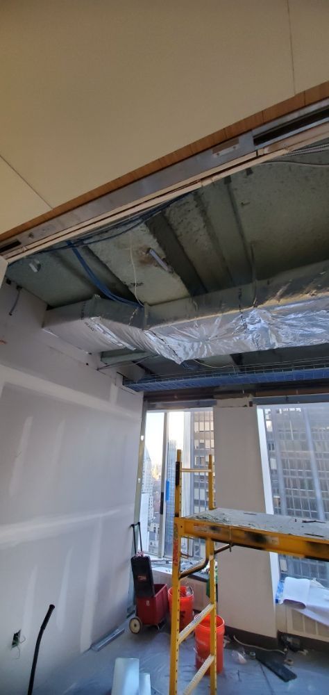 An unfinished office space with exposed ductwork, drywall, and a scaffolding.