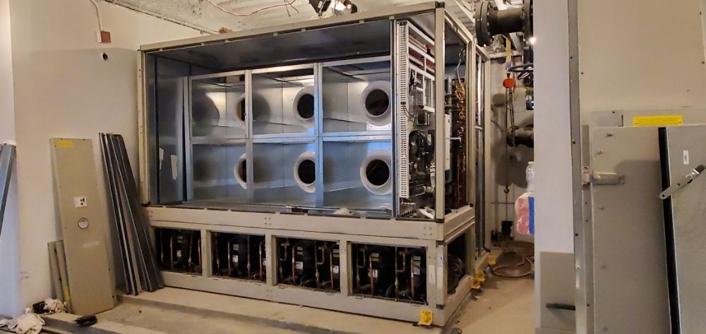 Large industrial air conditioning unit, metal frame, multiple round vents, unfinished construction setting.