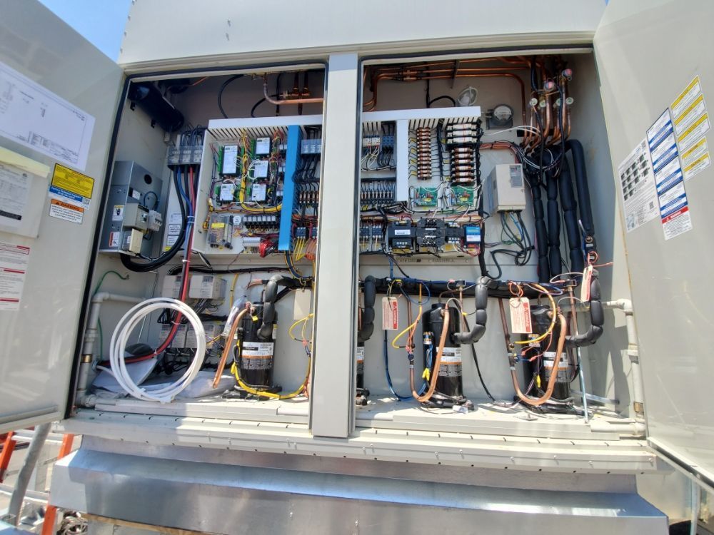 Open cabinet reveals HVAC components: electrical panels, copper tubing, compressors, and wiring.