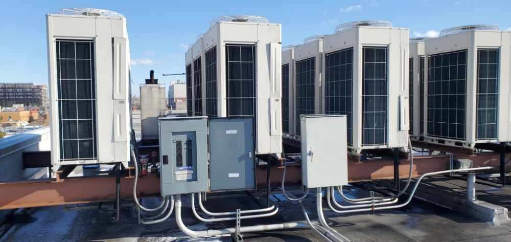 Rooftop HVAC units and electrical boxes, with conduit, against a blue sky.