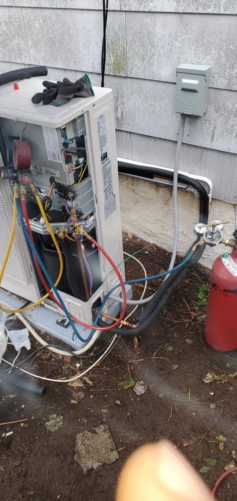 HVAC unit being serviced. Red and blue hoses connected to a red tank, near a gray electrical box.