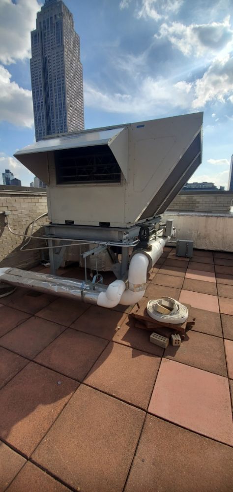 Rooftop HVAC unit on a tiled surface with a tall building in the background against a blue sky.