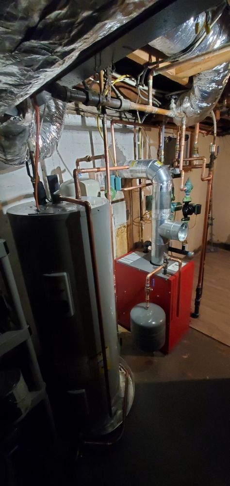 Basement with heating system components, including a water heater, boiler, and copper pipes.