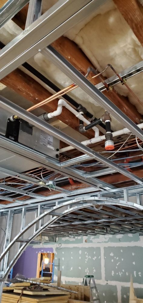 Construction site ceiling with metal framework, pipes, and insulation visible.