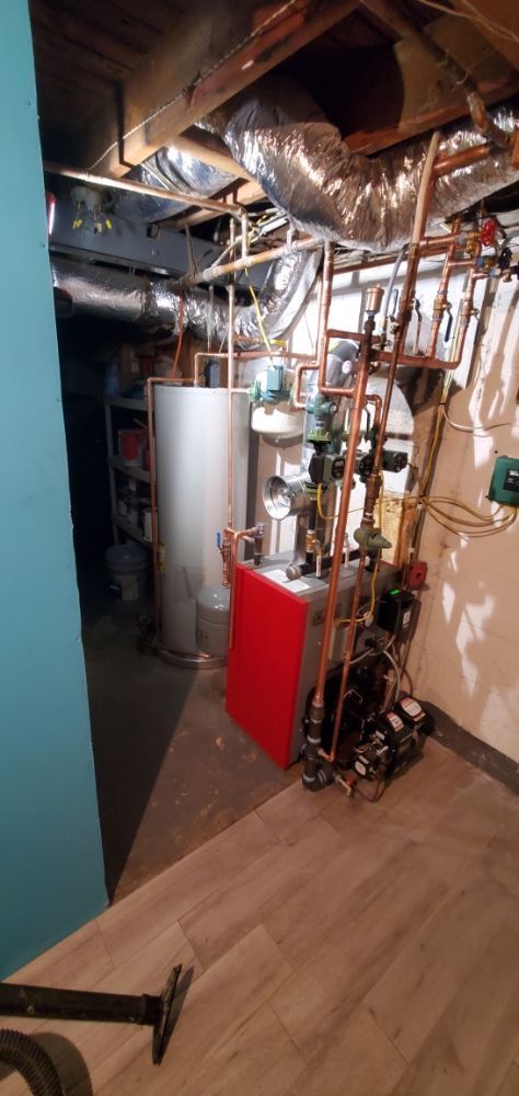 A basement utility room with a water heater, red cabinet, and copper piping.