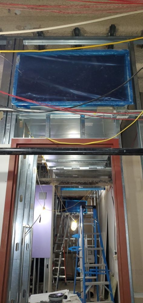 Interior view of a construction site with a large, covered object in a recessed space;metal framing; ladders; exposed wiring.