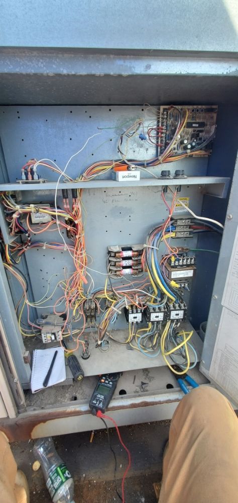 An open electrical panel with wires and components. A technician is working with tools.