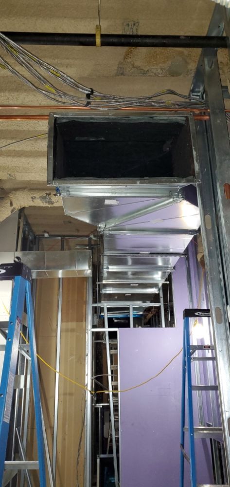 Construction site with ductwork, electrical wires, and purple drywall. Two ladders visible.