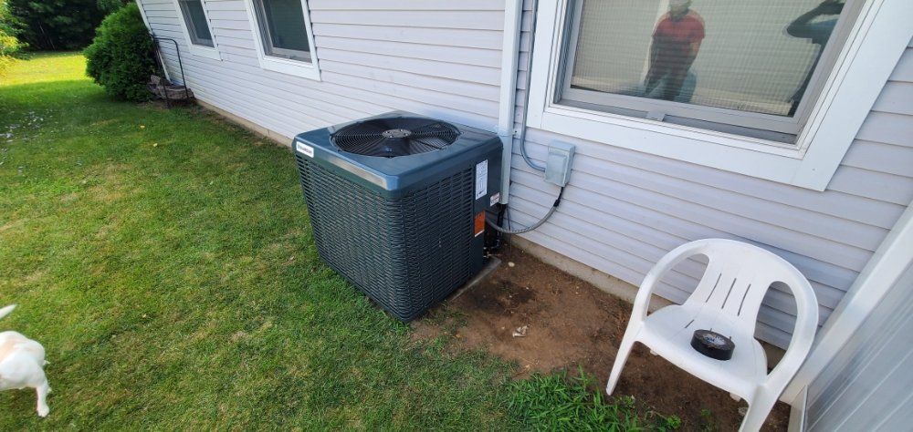 An air conditioning unit next to a house with a white chair in the grass.