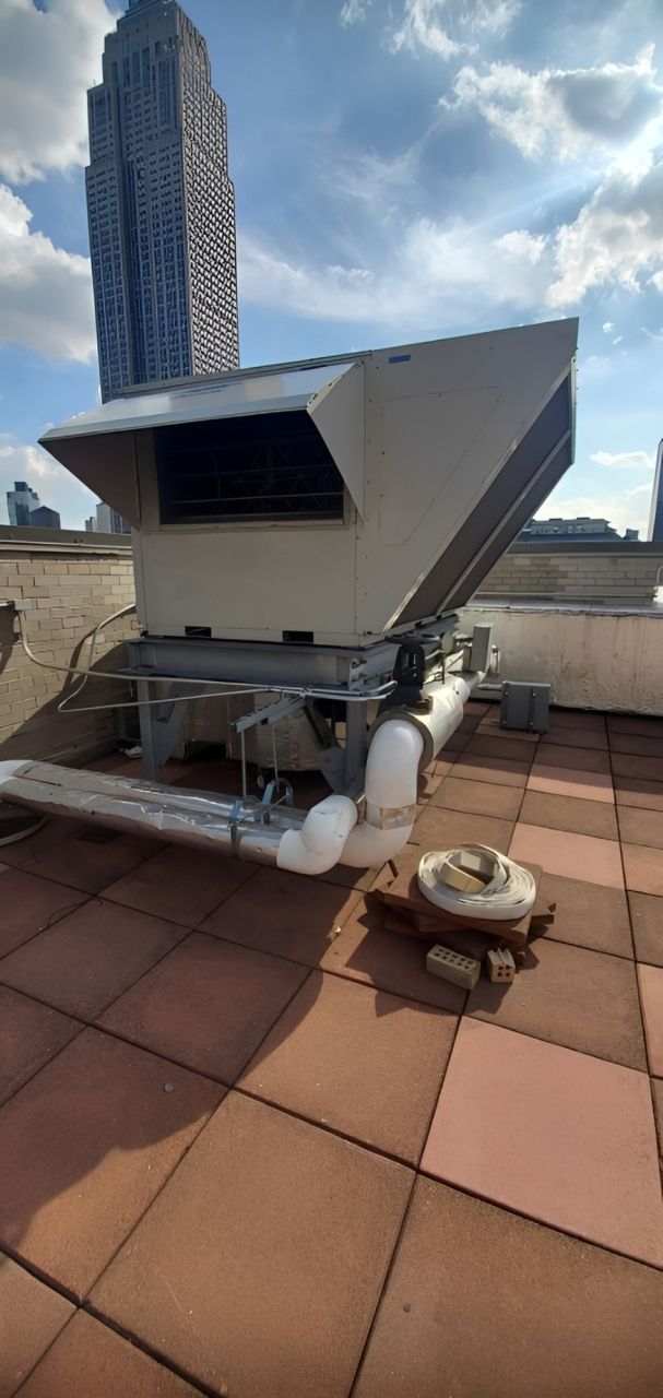 Three outdoor air conditioning units on a rooftop with a city skyline in the background.
