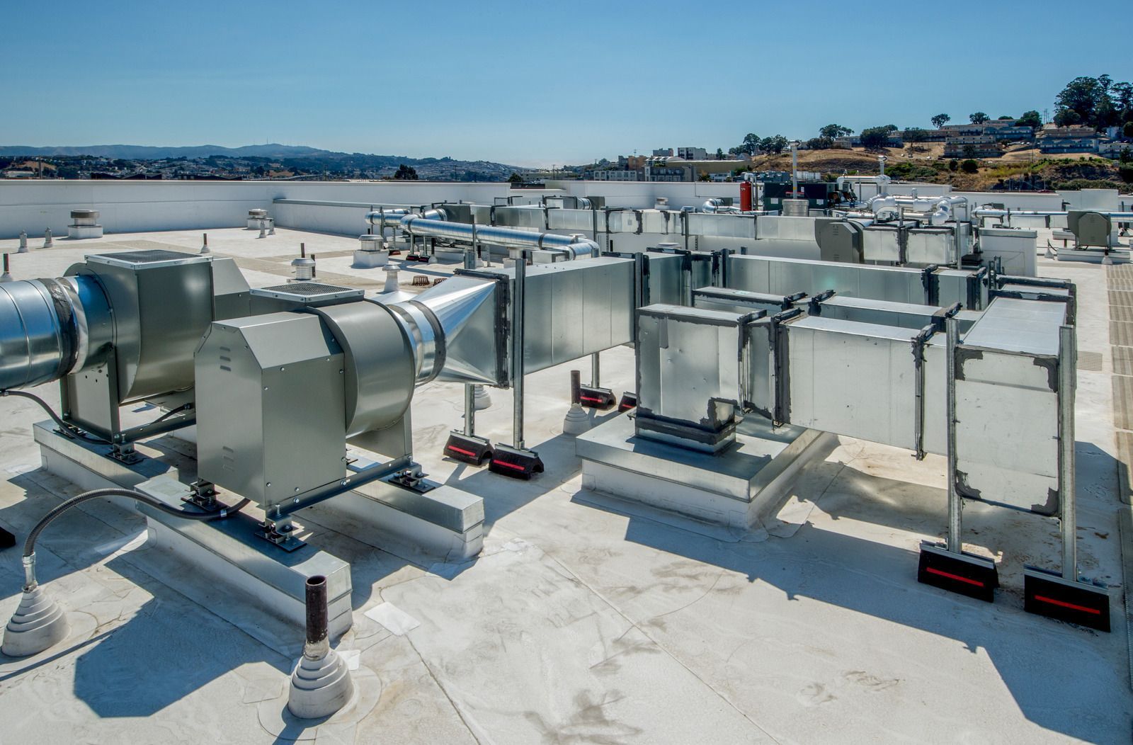 HVAC equipment on a white rooftop under a blue sky, with a distant cityscape.