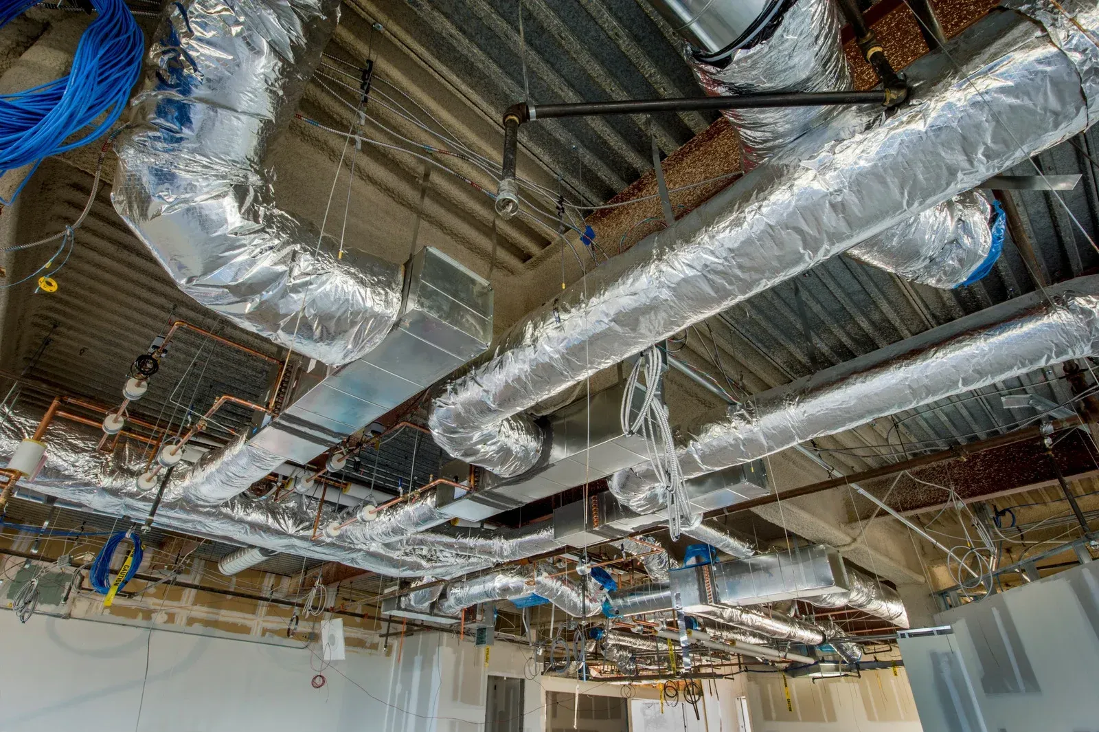 Three outdoor air conditioning units on a rooftop with a city skyline in the background.