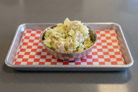 A bowl of mashed potatoes with garlic and basil on a table.