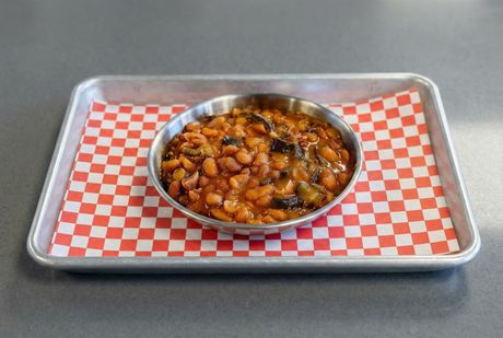 A bowl of baked beans with a wooden spoon on a table.