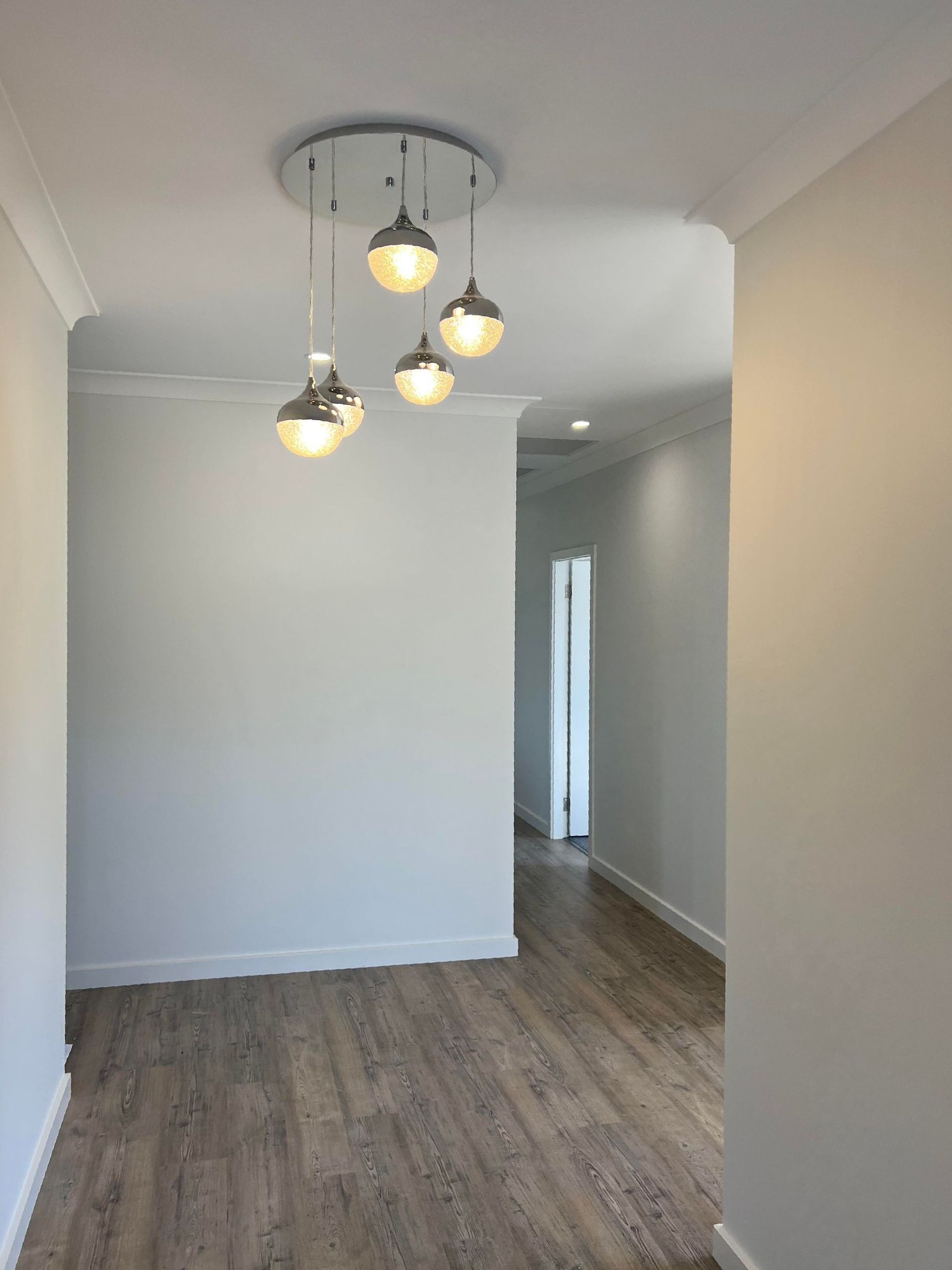An interior hallway with wood flooring, white walls, and a chrome chandelier — Col Groves Electrics Pty Ltd in Ballina, NSW