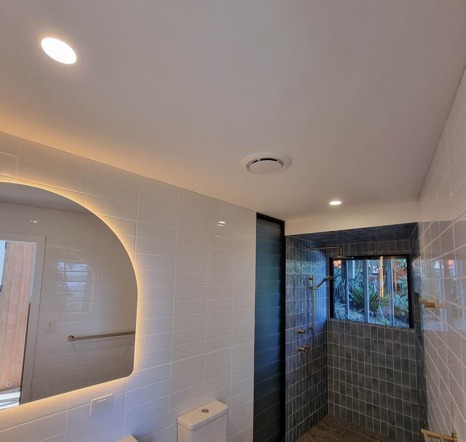Modern bathroom with a round mirror, shower stall, and white tile walls — Col Groves Electrics Pty Ltd in Ballina, NSW