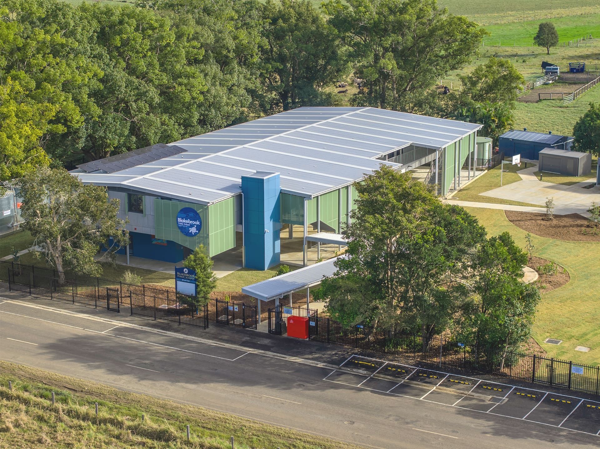 Building with solar panels on roof, blue and green exterior, near trees and field — Col Groves Electrics Pty Ltd in Ballina, NSW