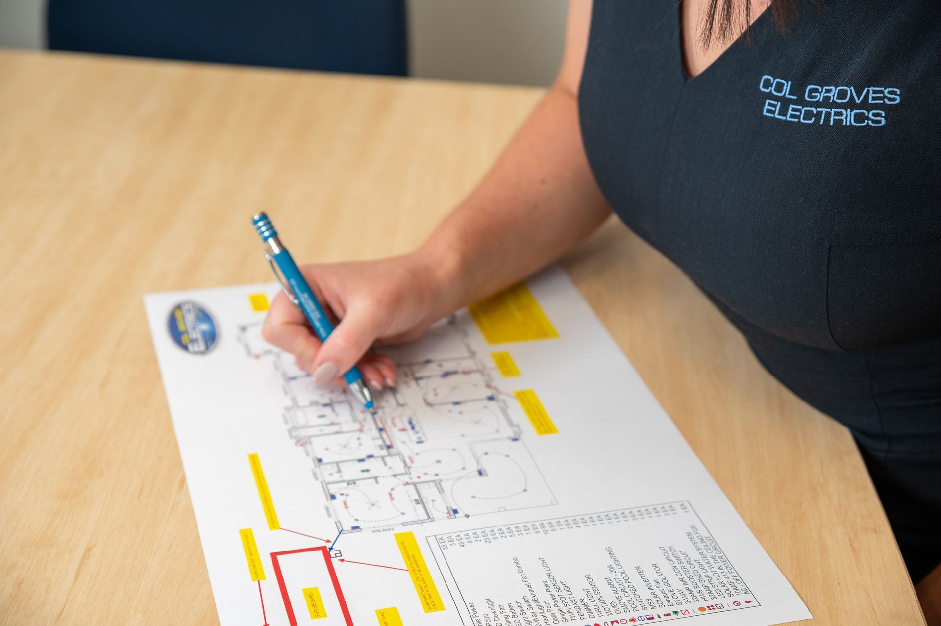 Woman Writing on a House Plan on a Wooden Table — Col Groves Electrics Pty Ltd in Ballina, NSW
