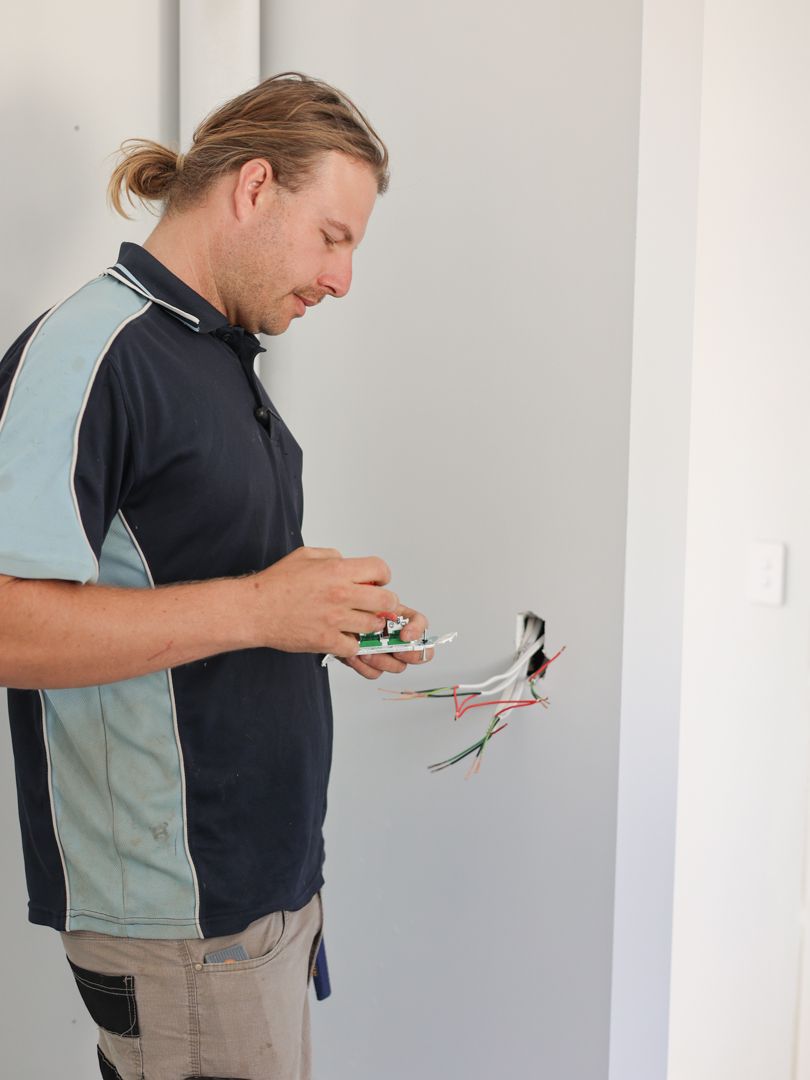 Man with ponytail wiring electrical outlet on gray wall — Col Groves Electrics Pty Ltd in Ballina, NSW