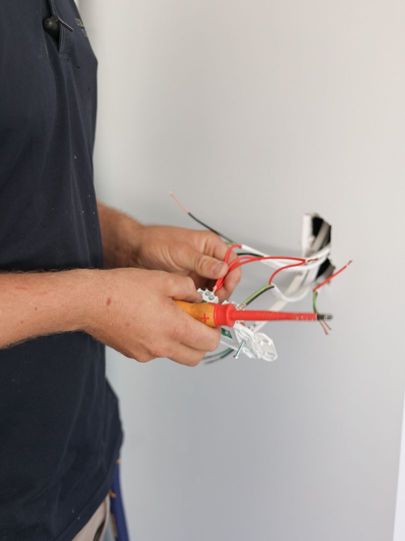 Person using a screwdriver to work on electrical wiring inside a wall — Col Groves Electrics Pty Ltd in Ballina, NSW
