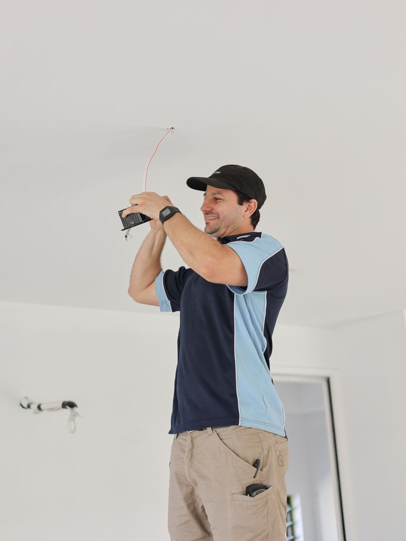 Man in work clothes installing electrical wiring on a white ceiling — Col Groves Electrics Pty Ltd in Ballina, NSW