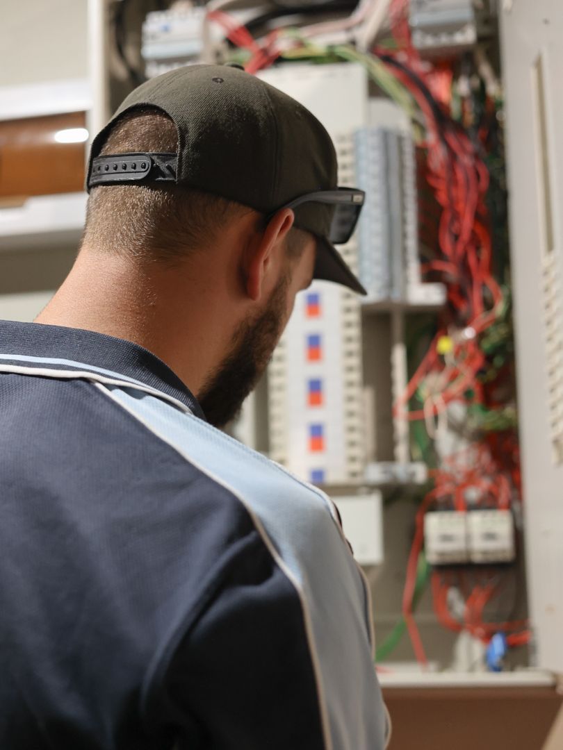 Man in cap working on electrical panel, examining wires — Col Groves Electrics Pty Ltd in Ballina, NSW