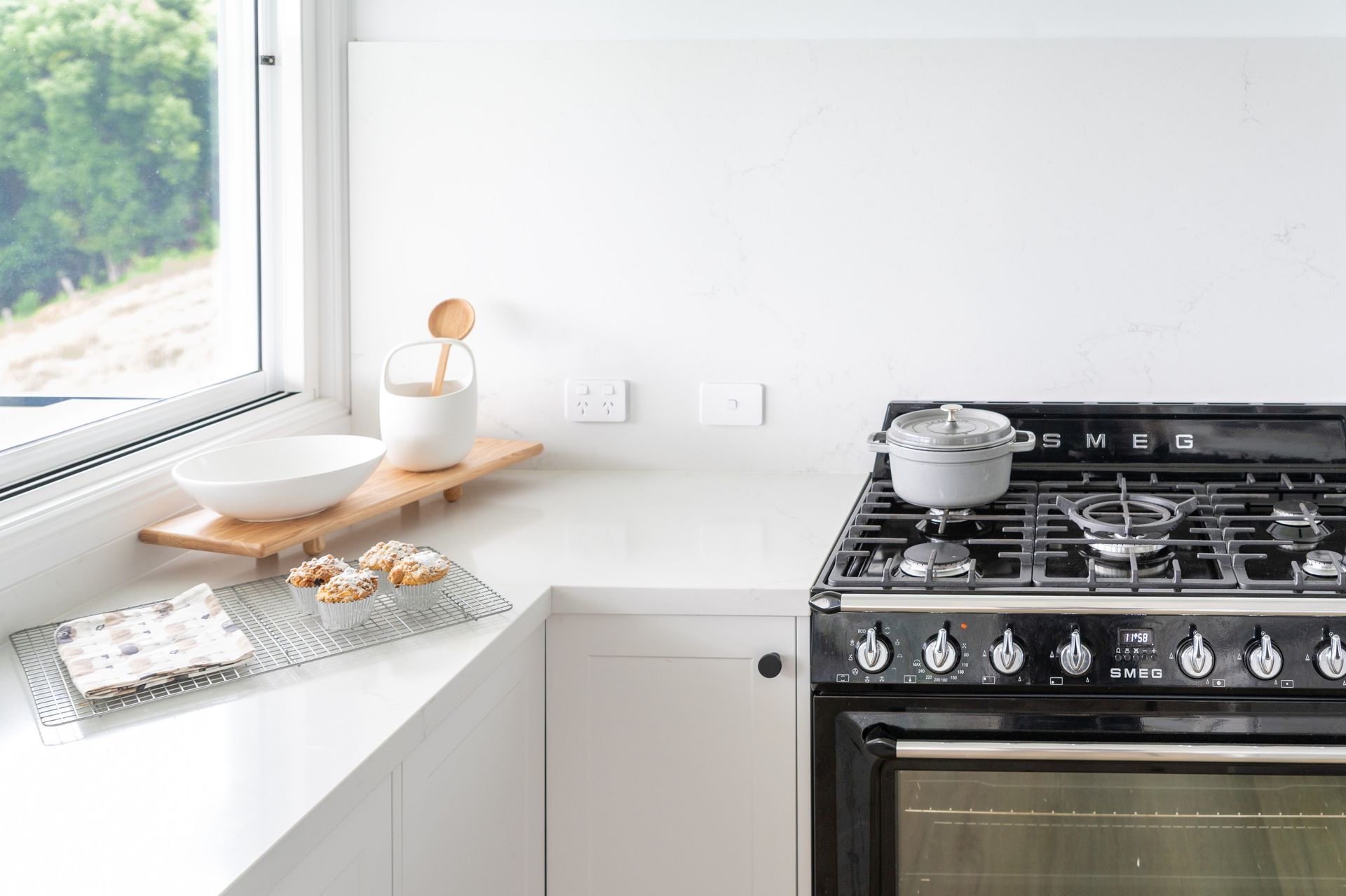 White kitchen with black stove; cookies, bowl, and jar on counter near a window.