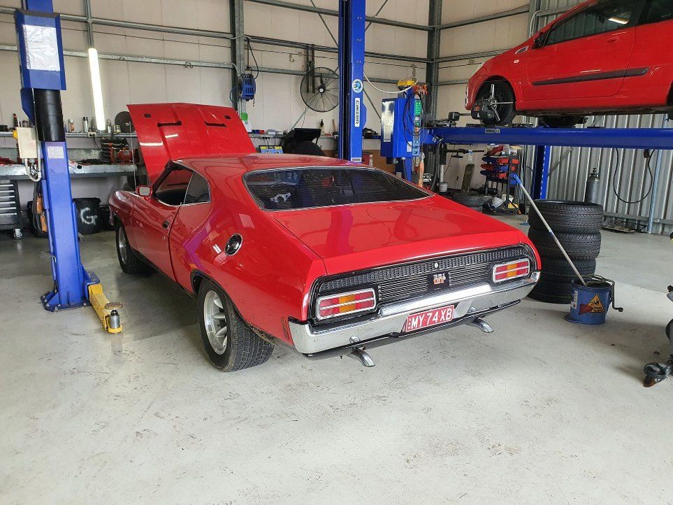 A Red Car With the Hood Up is on a Lift in a Garage — All Care Car Services Kumho Tyre Platinum Dealer in Kurri Kurri, NSW