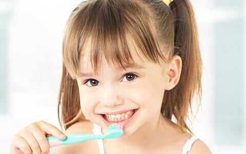 Oral Exams — Kid Smiling While Brushing Her Teeth in Erie, PA