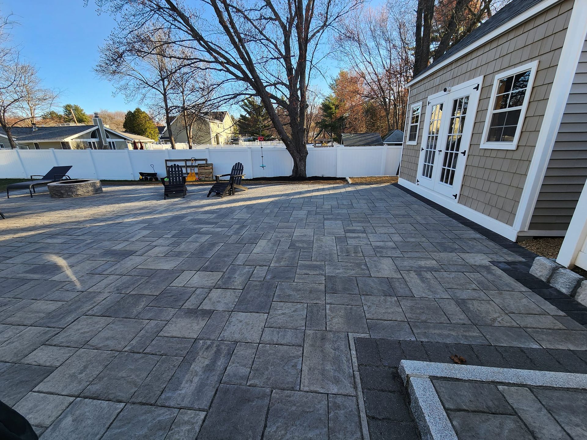 Large paver patio with shed, fire pit, and fence in a backyard setting.
