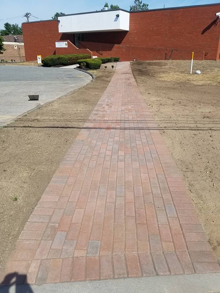 Brick walkway leading to a brick building. The walkway is surrounded by newly graded lawn