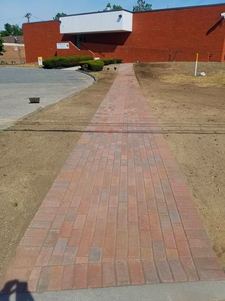 Brick paver walkway leading to a red brick building with white trim.