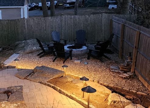 Backyard fire pit area with Adirondack chairs, low outdoor landscape lighting, and stone patio.