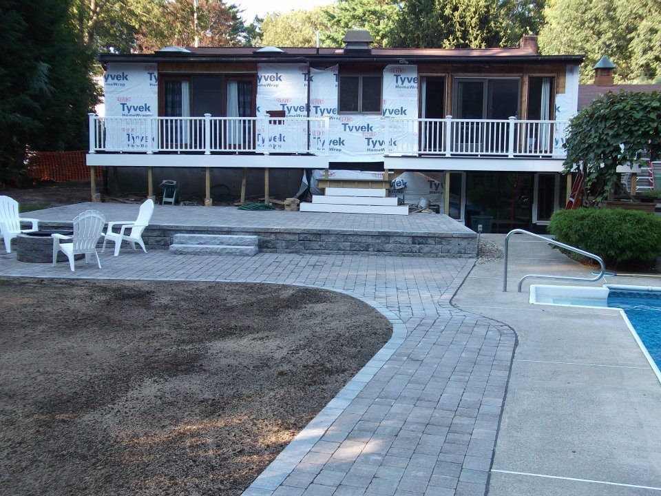 House under construction with a new raised patio, steps, and paver walkway leading to the pool. 