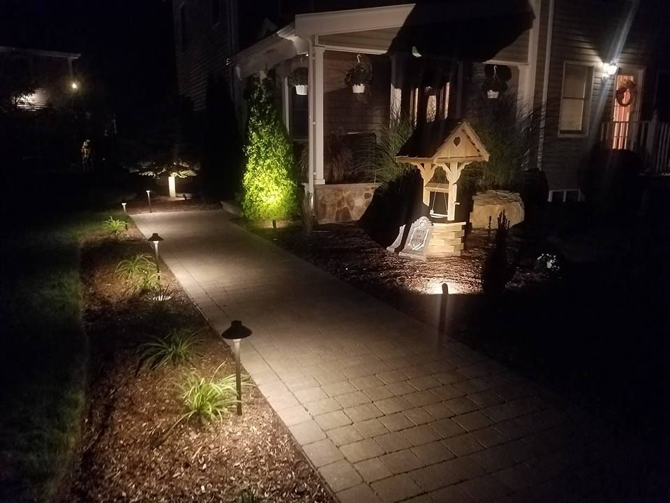 Lit walkway leading to a house at night, with path lights and a decorative well.
