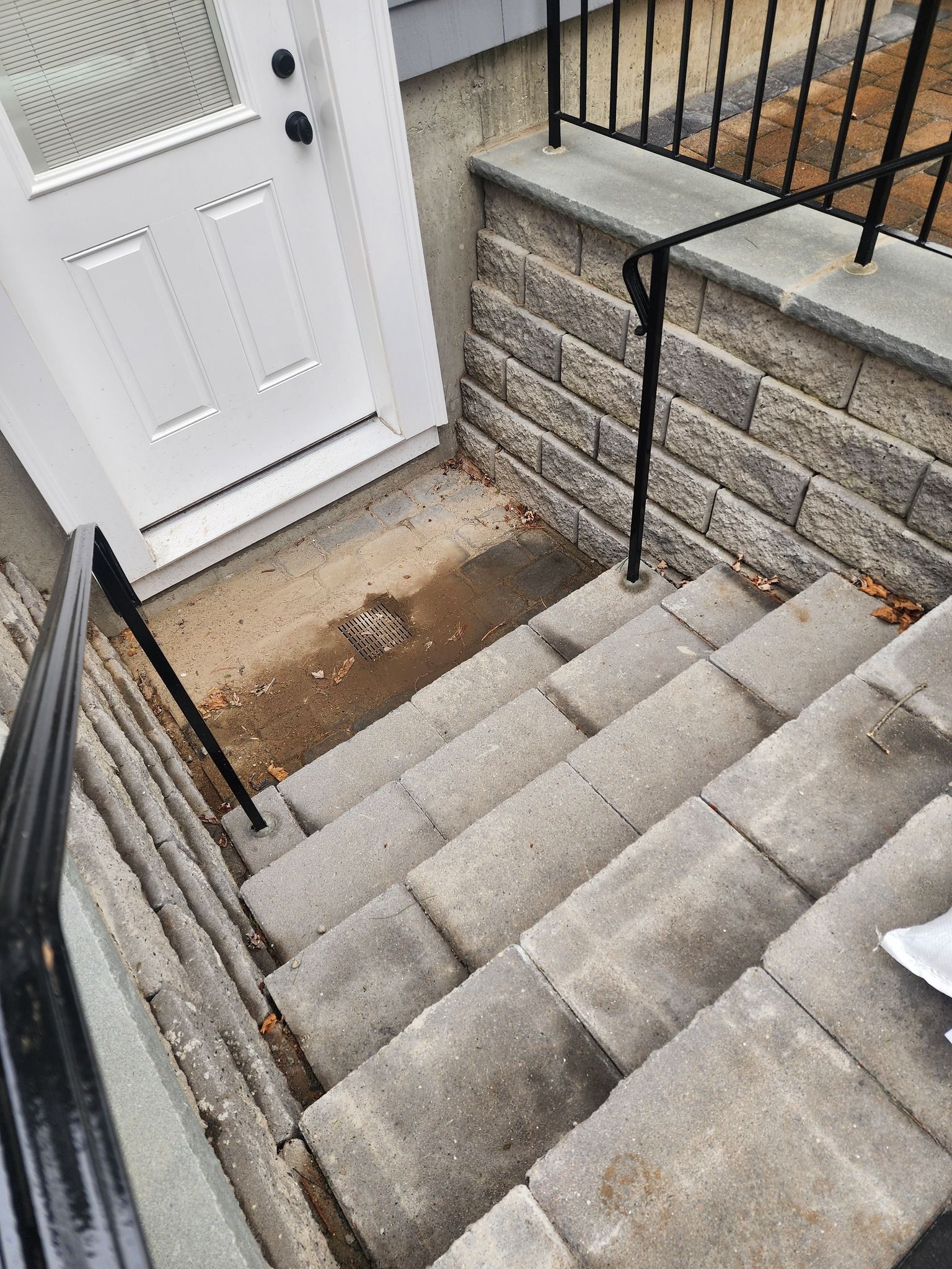 Granite steps leading down to a front door with a black handrail and a small paver landing area.