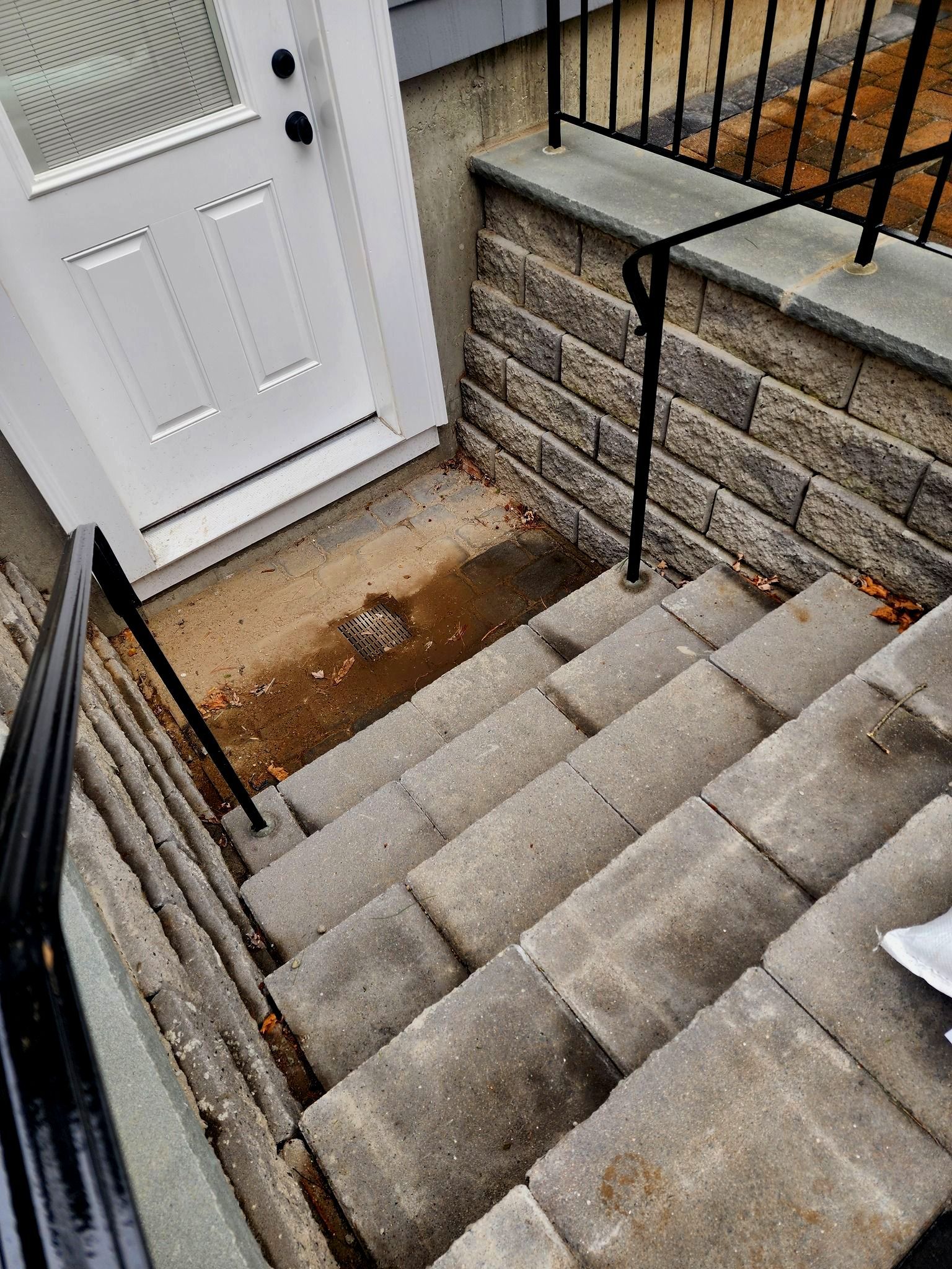 Concrete steps leading down to a front door with a metal railing.