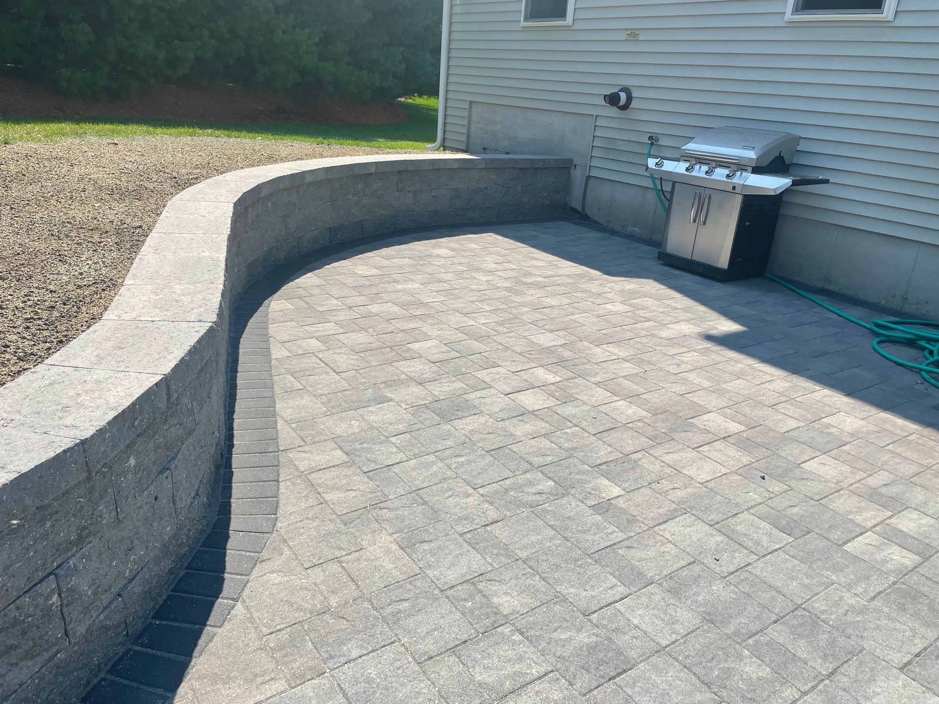 Paver patio with a custom curved retaining wall and grill against a light gray house