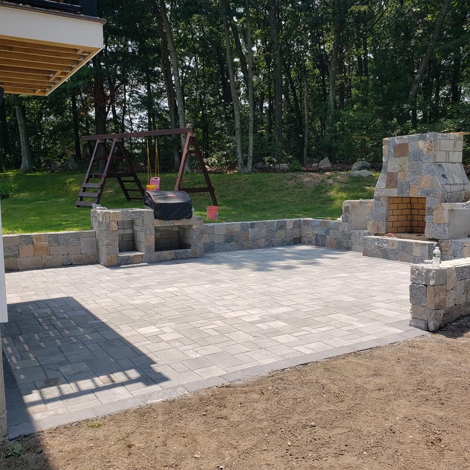Hardscaping project in Burlington, MA. Stone wall, patio, outdoor kitchen, and fire pit installation.