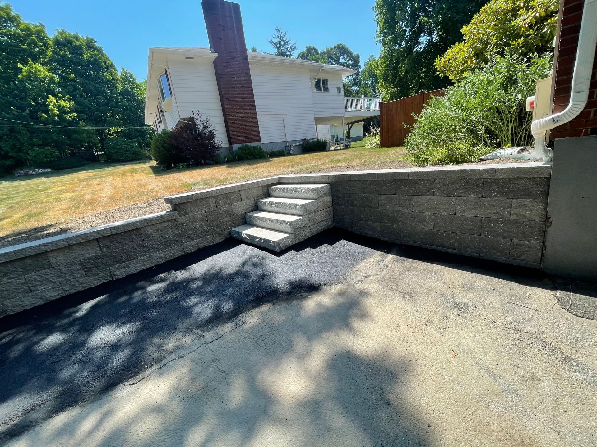 Granite steps leading up to a house with a new retaining wall, set on asphalt and grass.